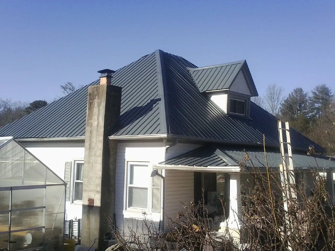 Dark blue standing seam metal roof on a white farmhouse with dormer — Slate & Tile Roof Repair by Roofing Brothers in Saint Marys