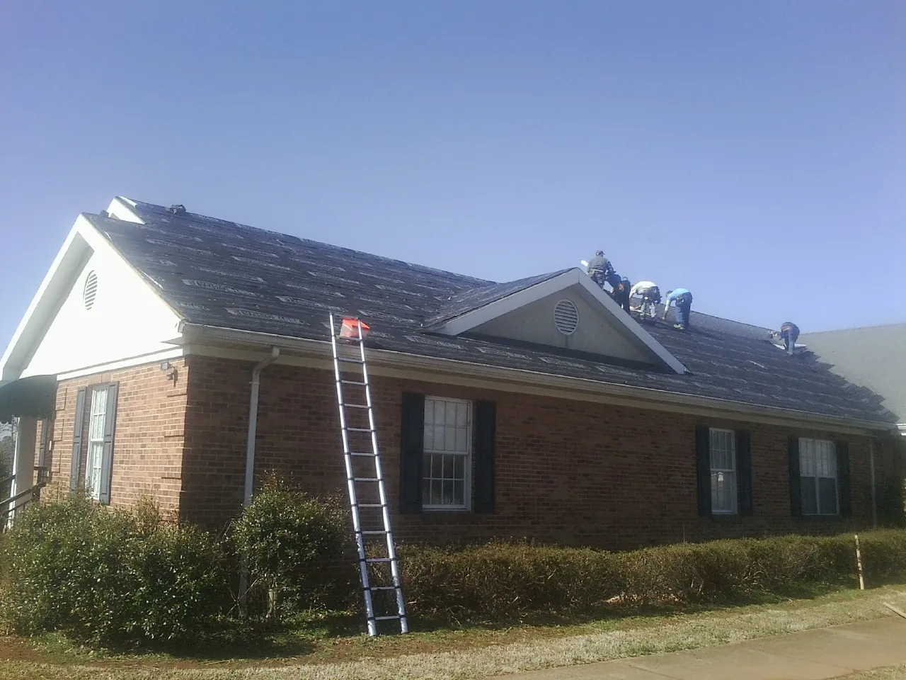 Crew tearing shingles off a brick ranch roof with a ladder set — Emergency Roof Repair work by our crew in Saint Marys