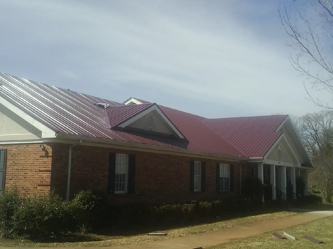 Red metal roof with gabled entries on a long brick building, from a Hail Damage Roof Repair job in Saint Marys
