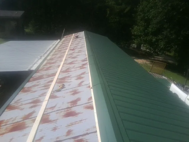 Old rusted panels beside newly installed green metal roofing — Wind Damage Roof Repair by Roofing Brothers in Saint Marys