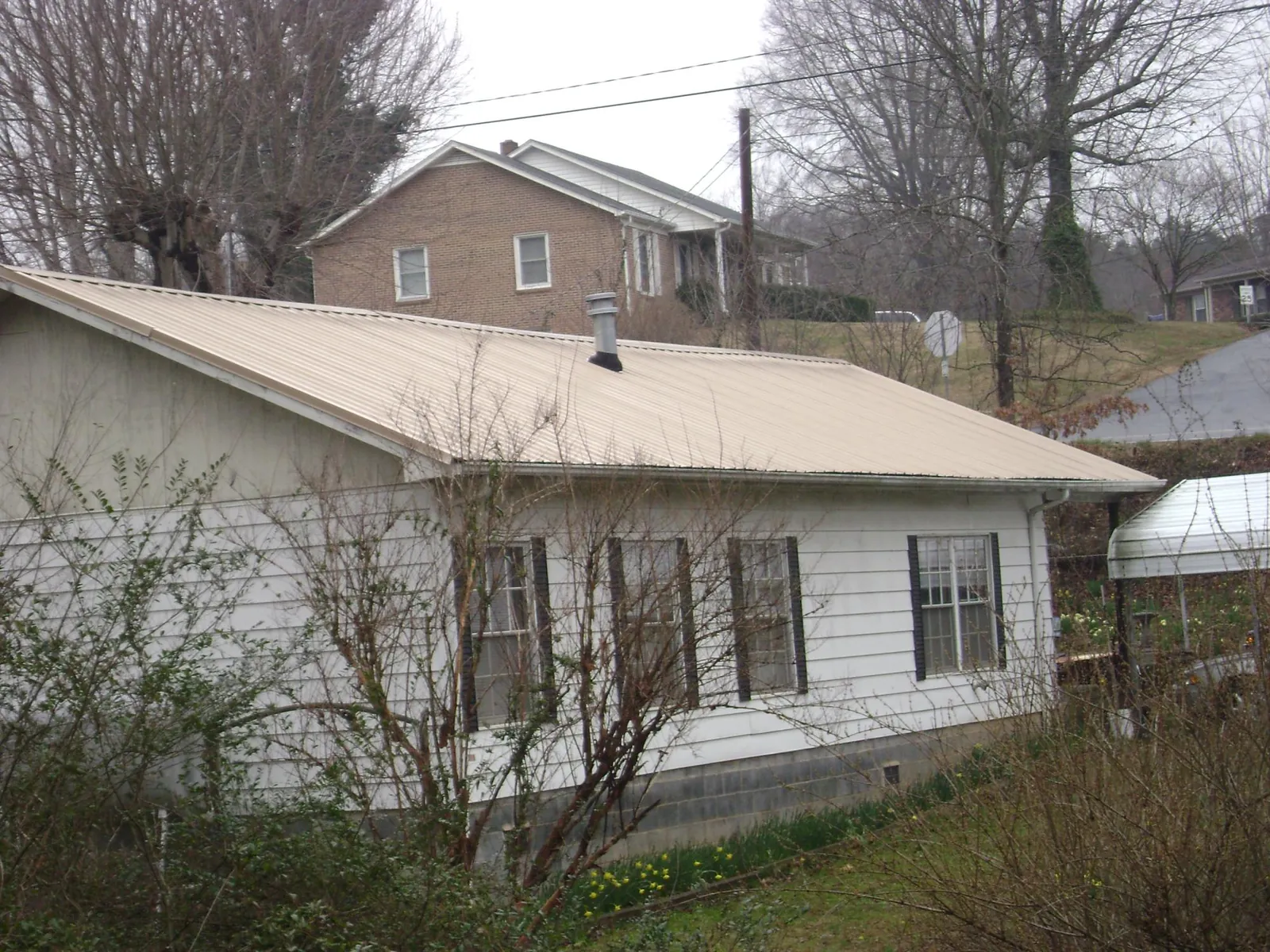 Tan metal roof on a white sided house set into a hillside — Commercial Roofing by Roofing Brothers in Saint Marys